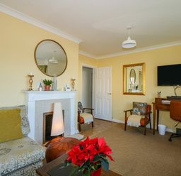 A living room with a fireplace a sofa a desk with a chair and a wall mounted television at See The Sea in Hunstanton