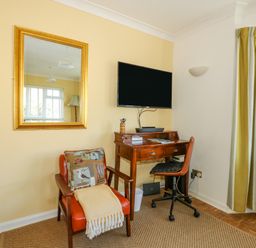 A corner with a wooden desk and chair under a wall-mounted TV and an armchair with cushion and throw at See The Sea in Hunstanton
