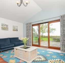 A living room with a blue sofa a patterned rug a white coffee table and sliding glass doors leading to a garden at Lambley View in Bude