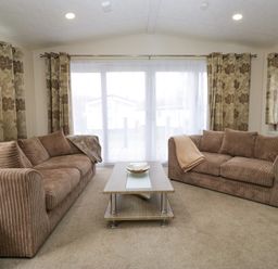 A living room with two brown sofas, a wooden coffee table, and floral curtains at 3 Yealands in Carnforth