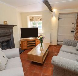 A living room with two sofas a wooden coffee table with flowers a television on a wooden stand a fireplace and a door at 5 Packhorse in Purton