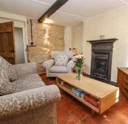 A living room with patterned sofa armchair wooden coffee table with flowers and board games fireplace and television at 5 Packhorse in Purton