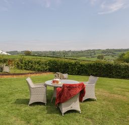 An outdoor seating area with a round table and four chairs on grass with a red blanket and cups at The Hayloft in Stockland Honiton