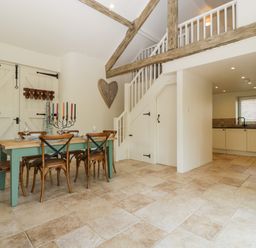 A dining area with a wooden table and chairs next to a staircase in an open kitchen space at The Hayloft in Stockland Honiton