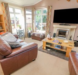 A living room with leather sofas a wooden coffee table a fireplace and a wall mounted TV at Mallard Lodge in Carnforth