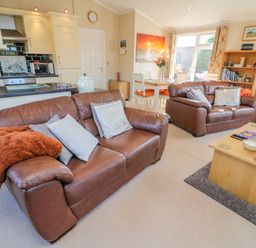 A living room with two brown leather sofas a wooden coffee table a bookshelf and a dining area with a table and chairs at Mallard Lodge in Carnforth