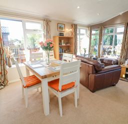 A dining table with four chairs and a vase of flowers next to a brown leather sofa in a living room at Mallard Lodge in Carnforth