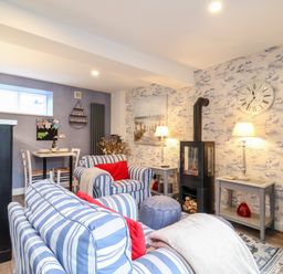 A living room with striped sofas red cushions a wood stove and small dining table at Tower End Cottage in Melton
