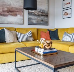 A yellow sectional sofa with various pillows and a wooden coffee table with books and decor at Porth Beach Villa in Porth near Newquay