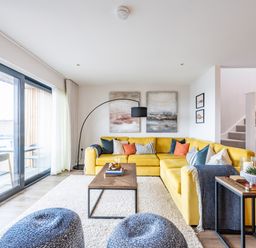 A living room with a yellow sectional sofa and a wooden coffee table at Porth Beach Villa in Porth near Newquay