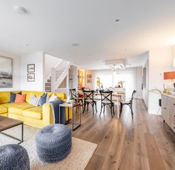 An open living and dining area with a yellow sofa, black chairs, wooden table, and staircase at Porth Beach Villa in Porth near Newquay