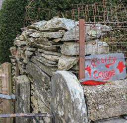 A stone wall with a metal gate and a sign reading Quarry Cottage in front of a white building with a red door at Quarry Cottage in Blaenau Ffestiniog