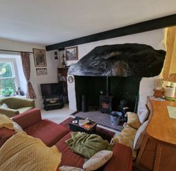A living room with a wood burning stove a red sofa a green armchair and a window at Quarry Cottage in Blaenau Ffestiniog