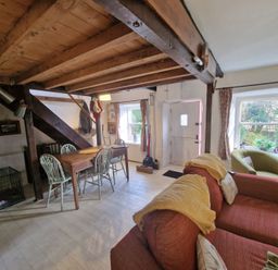 A living room with a red sofa green armchair wooden dining table and chairs under wooden ceiling beams at Quarry Cottage in Blaenau Ffestiniog