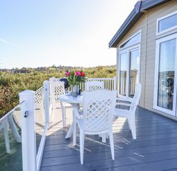 An outdoor deck with a white table and four white chairs with flowers on the table at Cherry Lodge in Teigngrace near Newton Abbot
