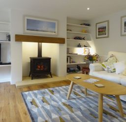A living room with a wood stove fireplace a wooden coffee table white sofa and built-in shelves at Fiddlesticks Cottage in Beaminster