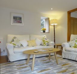 A living room with white sofas a wooden coffee table patterned cushions a floor lamp and flower arrangements at Fiddlesticks Cottage in Beaminster