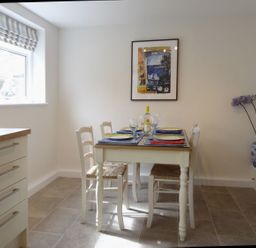 A dining area with a table set for four people next to a window and a blue and white vase with flowers at Fiddlesticks Cottage in Beaminster