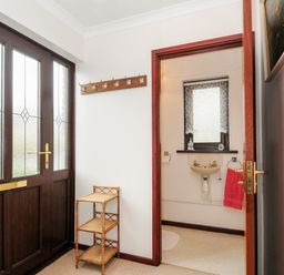 An entrance area with a wooden door a small shelving unit and a coat rack leading to a bathroom with a sink and a window at St Albans in Boscastle
