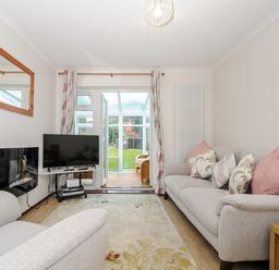 A living room with two sofas, a TV, a fireplace, a wall mirror, and glass doors leading to a garden at St Albans in Boscastle