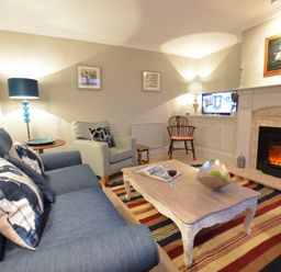 A living room with a blue sofa and armchair a wooden coffee table a fireplace and a television at Crabbe Corner in Aldeburgh