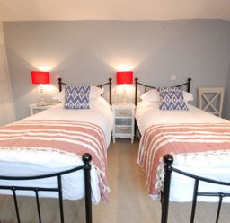 A bedroom with two single beds a bedside table with lamps and pillows at Crabbe Corner in Aldeburgh