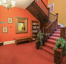 A staircase with red carpet next to a wooden bookshelf and a wooden table with a wall mirror at Peak View in Keswick