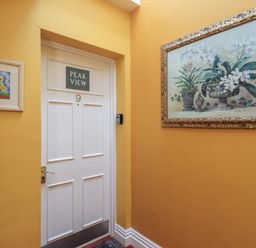 A hallway with a white door numbered nine and Peak View sign with yellow walls and flower paintings at Peak View in Keswick
