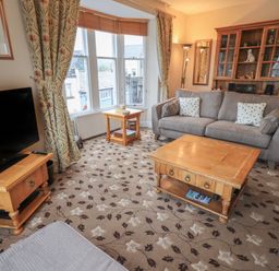 A living room with a gray sofa wooden coffee tables a TV on a wooden stand and floral carpet at Peak View in Keswick