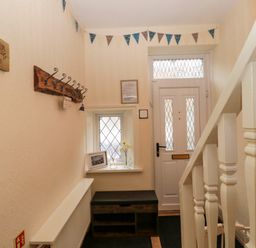 An entryway with a white door a window with diamond panes a wooden bench a coat rack and stairs at Bonnies Retreat in Amble
