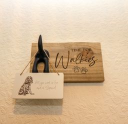 A wall with a wooden plaque that says Time for Walkies and a hanging sign with a dog illustration and text at Bonnies Retreat in Amble
