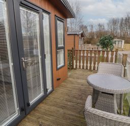 An outdoor wooden deck with a round table and two wicker chairs outside a building with glass doors and windows at 24 Sherwood in Carnforth