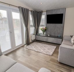 A living room with grey sofas a wall-mounted television grey curtains and a rug at 24 Sherwood in Carnforth