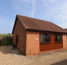 A single story house with brick and wood panel exterior and a tiled roof surrounded by a gravel driveway at Church View in Atwick