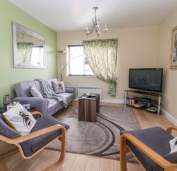 A living room with two armchairs, a sofa, a coffee table, a television, a standing lamp and a window with curtains at Church View in Atwick