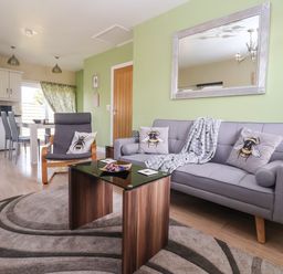 A living room with grey sofa and armchair with bee cushions and a wooden coffee table at Church View in Atwick
