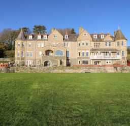 A large stone manor house with turrets and multiple windows facing a wide lawn at Bryn Mel Manor Straits View in Menai Bridge