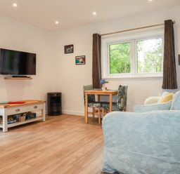 A living room with a sofa table and chairs a wall-mounted TV and a window at Pheasant View in Penelewey near Carnon Downs