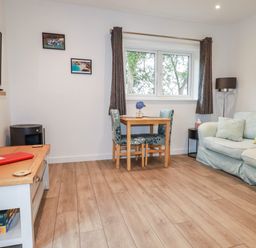 A living room with a light blue sofa a wooden table with two chairs a wall-mounted television and wooden flooring at Pheasant View in Penelewey near Carnon Downs