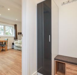 A room with a black and white wardrobe and a wooden bench with a cushion next to a living area with a small wooden table and two chairs at Pheasant View in Penelewey near Carnon Downs