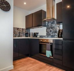 A kitchen with black cabinets a patterned tile backsplash a clock and kitchen appliances at Pheasant View in Penelewey near Carnon Downs