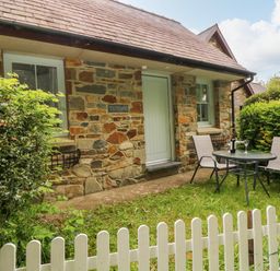 A stone cottage with two windows a door and outdoor table and chairs behind a white picket fence at Ty Rhydd in Newport Pembrokeshire