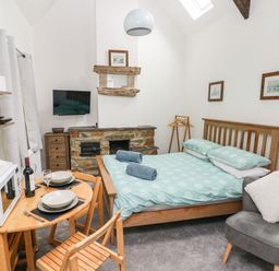 A bedroom with a wooden bed dining table with microwave and chairs a fireplace and a gray armchair at Ty Rhydd Newport Pembrokeshire