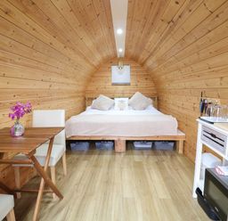 An arched wooden interior with a bed at the end a table with chairs on the left and a small kitchen area on the right at The Pod at Bank House Farm The Blythe near Hixon