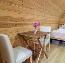 A wooden table with a vase of flowers and two white chairs next to a bed with cushions in a wooden room at The Pod at Bank House Farm The Blythe near Hixon