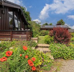 A garden with red flowers shrubs and stone steps beside a wooden house at Greengarth in Yanwath near Penrith