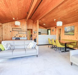 A living room with wooden walls and ceiling a gray sofa green dining chairs and a wooden dining table at Greengarth in Yanwath near Penrith