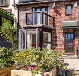 Front view of a brick house with glass balcony wooden planters with green plants and an open glass door at Yacht Haven View in Neyland