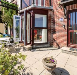 An outdoor patio area with a table and chairs next to a brick building with glass doors open at Yacht Haven View in Neyland
