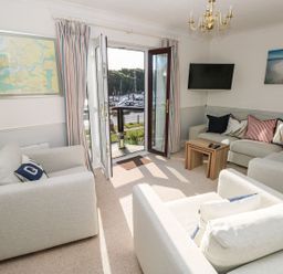 A living room with sofas a small wooden table a wall-mounted TV and open doors leading to a marina view at Yacht Haven View in Neyland